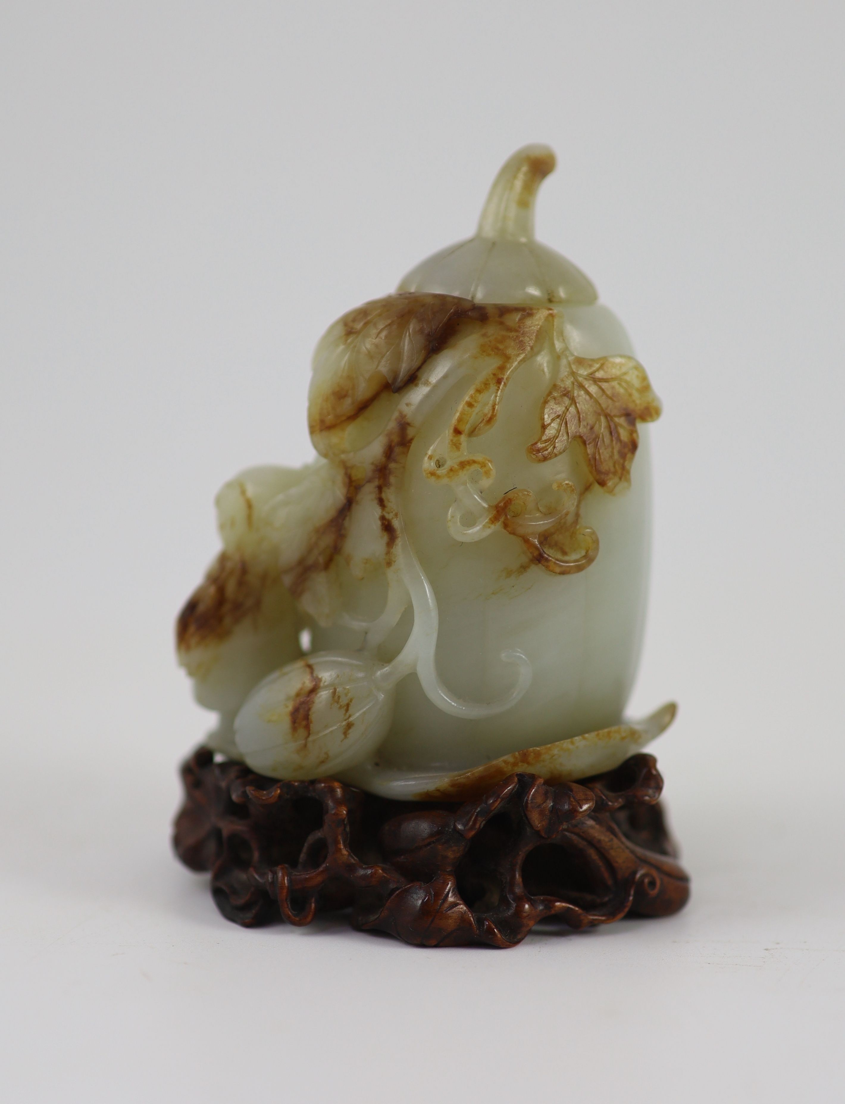 A Chinese pale celadon and russet jade 'boy' jar and cover, 8.3 cm high, the hardwood stand carved as a vine